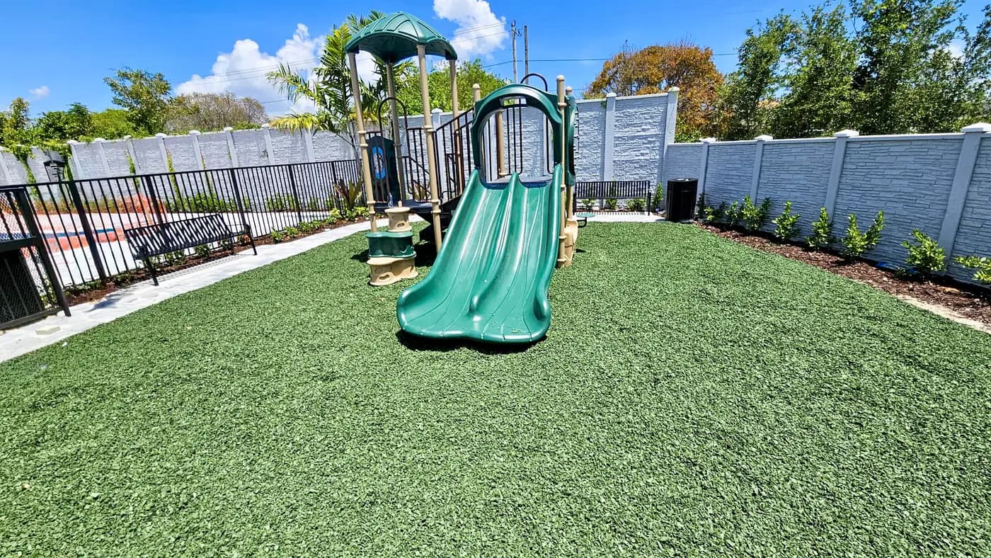 Green double slide unit on green rubber mulch in the walled Centris courtyard beside the pool