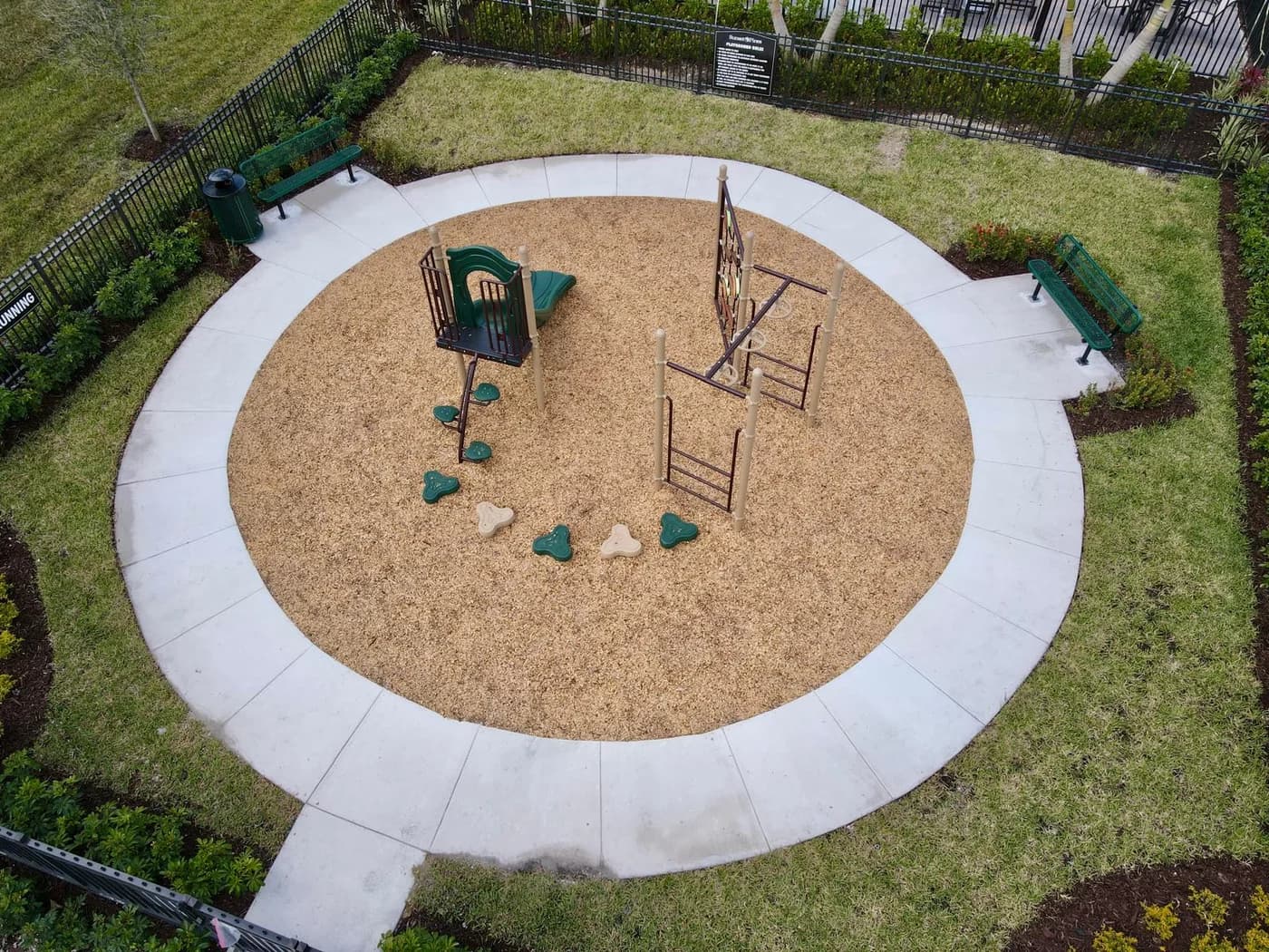 Aerial view of a circular playground with a green play system and climber on engineered wood fiber