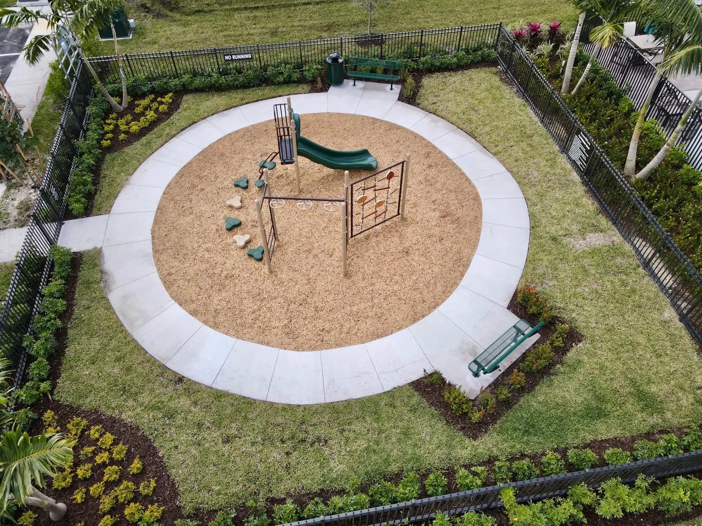 The fenced circular play area with benches and landscaping around the concrete border