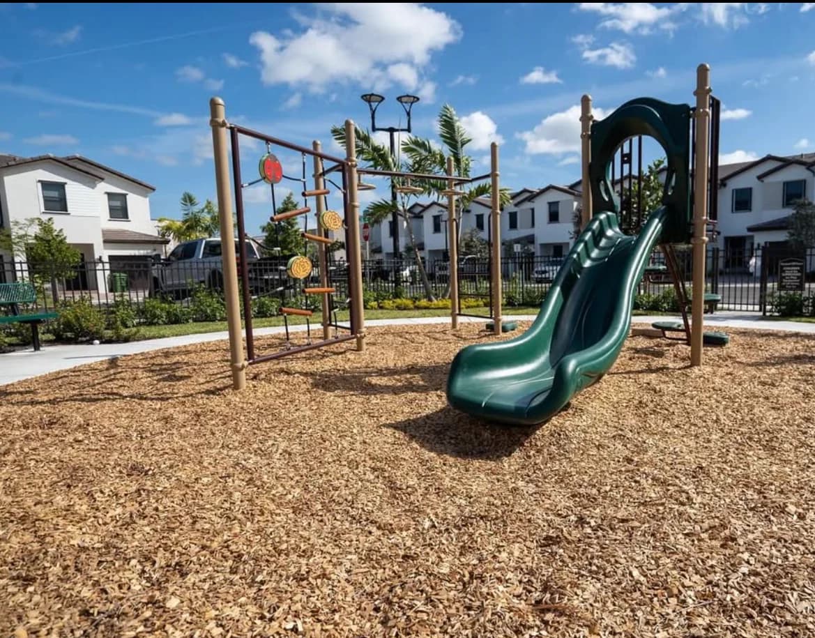 Playground with a green slide and climber on engineered wood fiber in a Pembroke Pines residential community