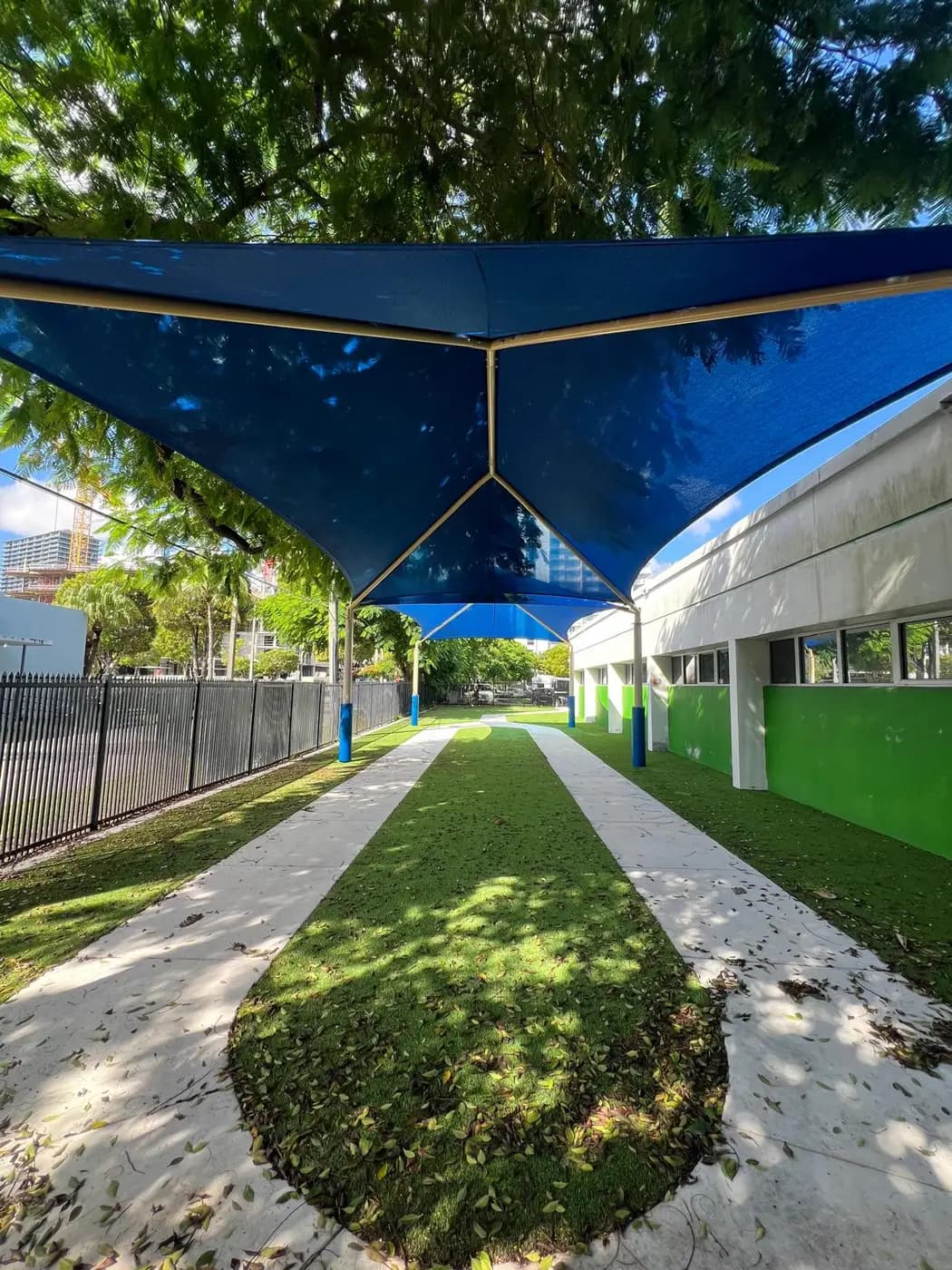 Blue double hip shade canopies over a turf walkway at a school campus