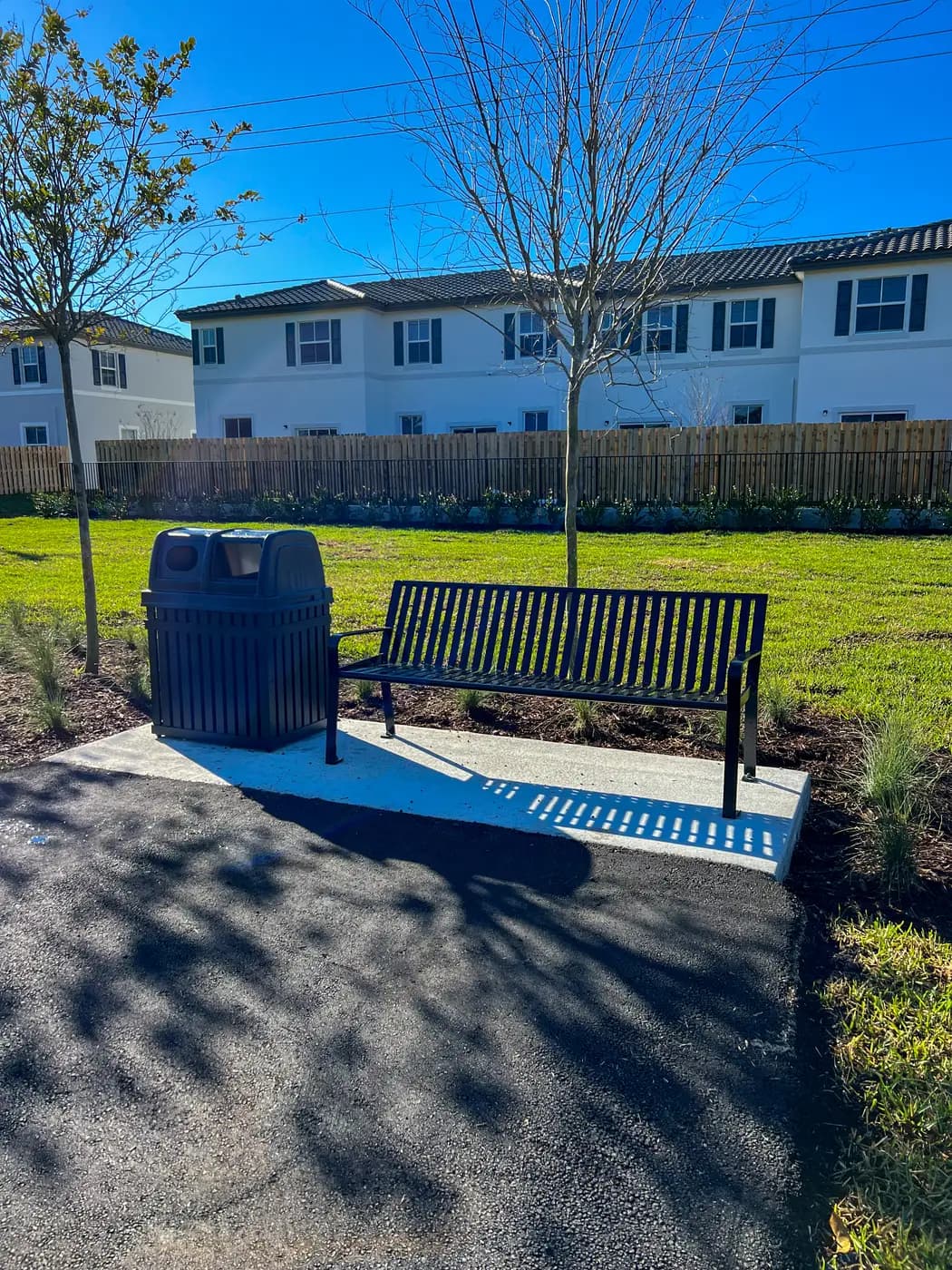 Black metal bench and trash receptacle in front of new townhomes